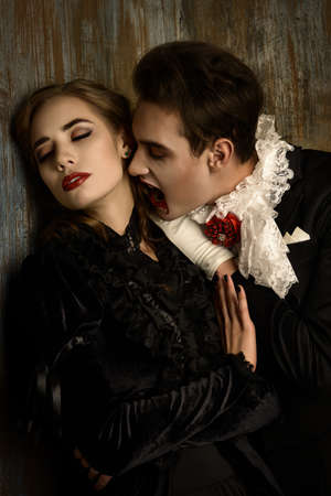 Bloodthirsty male vampire in medieval dress is biting a beautiful lady. Halloween.の写真素材