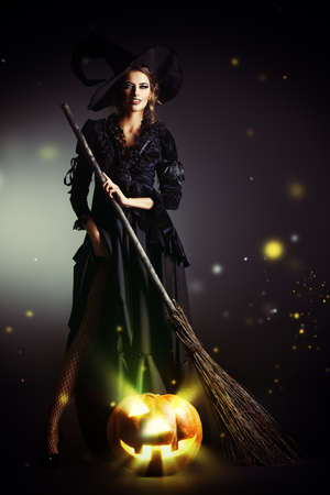 Gorgeous brunette witch with her broom over black background. Halloween.の写真素材