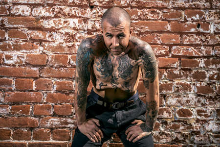 Portrait of a muscular man with tattoo standing on a street by a brick wall. Tattoo concept.の写真素材