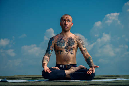 Yoga concept. Experienced yoga master meditates in the lotus position sitting on a roof over blue sky.の写真素材