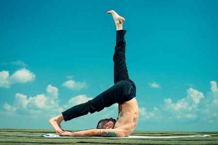 Yoga concept. Experienced yoga master performs various yoga poses on a roof over blue sky.