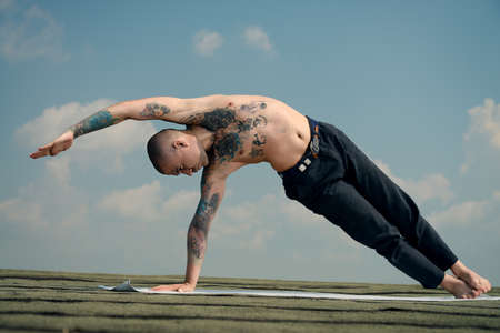 Yoga concept. Experienced yoga master performs various yoga poses on a roof over blue sky.の写真素材