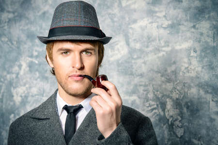 Handsome young man wearing classic hat and a coat smokes a pipe. Beauty, fashion.の写真素材