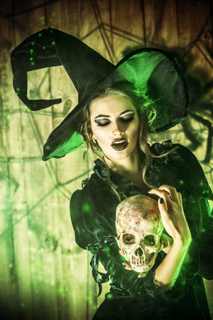 Frightening witch girl in medieval dress and a hat holding a skull in a mysterious abandoned house....