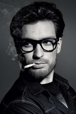 Black-and-white portrait of a smoking young man. Handsome young man thoughtfully and calmly smoking a cigarette. Men's beauty, fashion.の写真素材