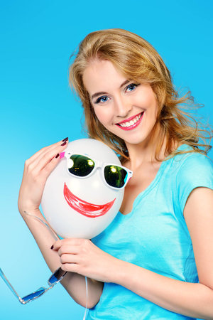 Pretty cheerful young woman in summer clothes posing with a balloon and sunglasses.の写真素材