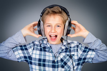 Cheerful teen boy listening to music in headphones and singing a song. Studio shot.