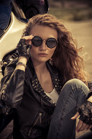 Sexual biker woman wearing black leather jacket sitting on her motorcycle on a highway. Beauty,...