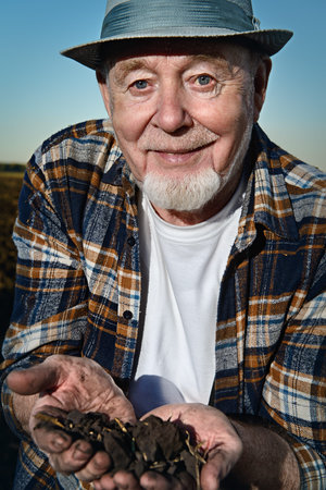 An elderly farmer holds a handful of fertile black soil in his hands and smiling. Agriculture, crop concept.の写真素材