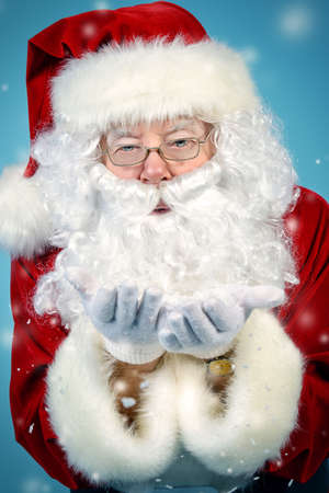 Good old Santa Claus blowing a snow over blue background. Snowfall, snowflakes. The magic of Christmas.の写真素材