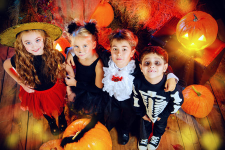 Cheerful children in halloween costumes celebrating halloween in a wooden barn with pumpkins. Halloween concept.の写真素材