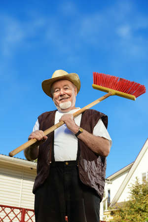 Raking in the garden. Happy senior man gardening in retirement.の写真素材