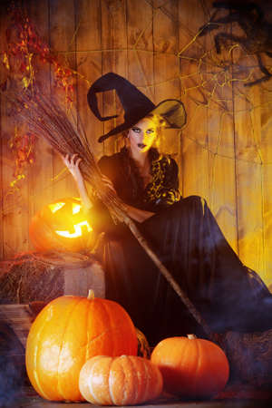 Beautiful fairy witch with her broom in a wooden barn with pumpkins. Halloween.の写真素材