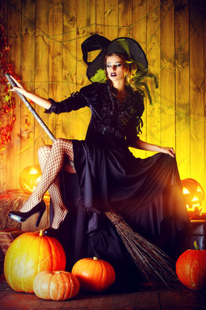 Beautiful fairy witch with her broom in a wooden barn with pumpkins. Halloween.