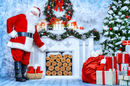 Traditional Santa Claus standing by the fireplace and Christmas tree in a beautiful room, decorated for Christmas.の写真素材