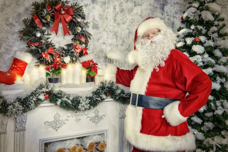 Jolly Santa Claus standing by the fireplace in a room, decorated for Christmas.