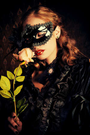 Charming mysterious girl in black mask and black medieval dress stands in a castle living room. Vampire. Halloween concept. Vintage style.の写真素材