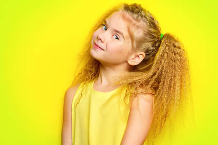 Joyful little girl with beautiful blonde hair over yellow background. Kid's style. Hairstyle.の写真素材