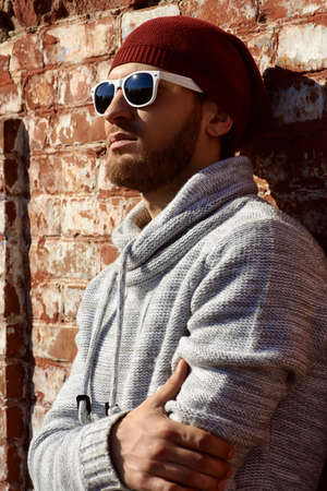 Handsome young man leaning against the brick wall on the street. Men's beauty, fashion.の写真素材