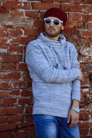 Handsome young man leaning against the brick wall on the street. Men's beauty, fashion.の写真素材