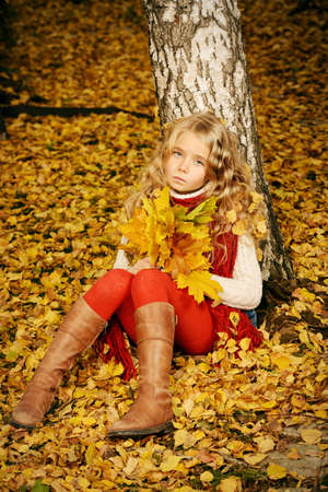 Pretty girl with a bunch of yellow leaves in the beautiful autumn park. Children's fashion.の写真素材