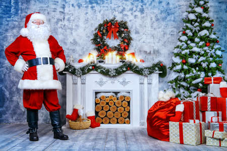 Traditional Santa Claus standing by the fireplace and Christmas tree in a beautiful room, decorated for Christmas.の写真素材