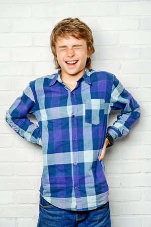 Portrait of emotional teenage boy standing by a white brick wall. Studio shot. Teen fashion.の写真素材
