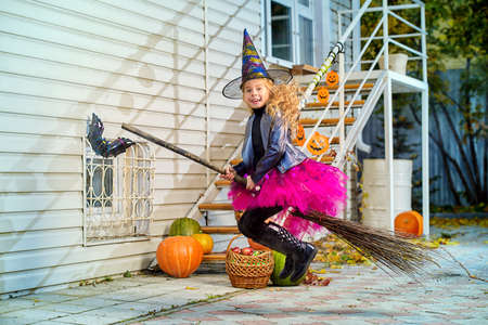 Pretty little girl in a costume of witch with her magic broom celebrating halloween. Trick or treat. Halloween party.の写真素材