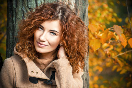 Romantic dreamy girl with beautiful red hair walks in autumn park. The mood of autumn, leaf fall. Autumn fashion.の写真素材