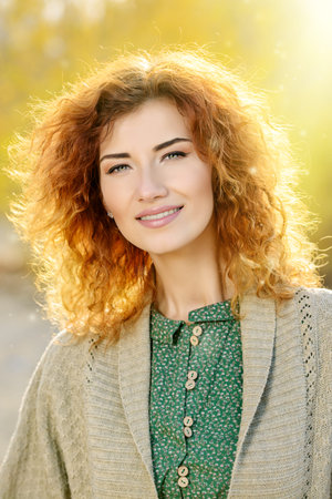 Beautiful dreamy girl with curly red hair walks in autumn park. The mood of autumn, leaf fall....
