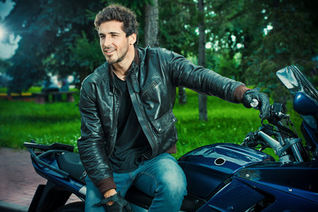 Sexy biker man wearing jeans and leather jacket sitting relaxed on his motorcycle.の写真素材