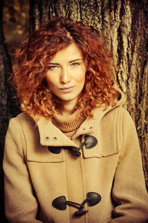 Romantic dreamy girl with beautiful red hair walks in autumn park. The mood of autumn, leaf fall. Autumn fashion.の写真素材