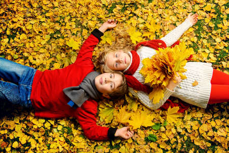 Two cheerful kids lying on a yellow leaves in a beautiful autumn park. Children's fashion. Autumn leaf fall.の写真素材