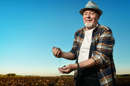 An elderly farmer standing in a plowed field. Agriculture, crop concept.の写真素材