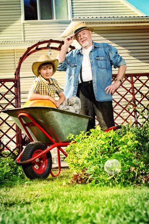 Happy grandpa and his grandson harvest of pumpkins in the garden. Sunny autumn day.の写真素材