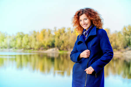 Autumn style. Beautiful happy young woman with bright foxy hair wearing black coat in the autumn park. Beauty, fashion.の写真素材