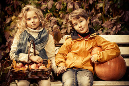 Happy romantic boy and girl sitting on a bench in a beautiful autumn park. Children's fashion. Autumn mood, halloween. Sepia.の写真素材