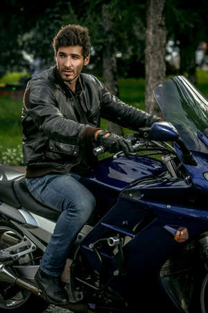 Sexy biker man wearing jeans and leather jacket sitting relaxed on his motorcycle.の写真素材