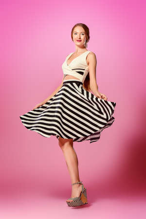 Beautiful happy young woman wearing skirt and top blouse alluring over pink background. Fashion studio shot. Full length portrait.の写真素材