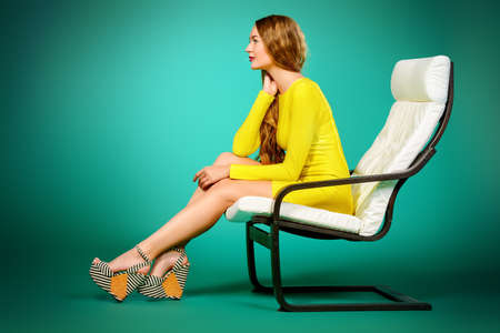 Sexy female model with beautiful long hair sitting on a chair. Beauty, fashion concept. Interior, furniture.の写真素材