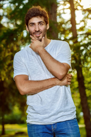 Smiling young man standing relaxed on a green lawn at a summer park.の写真素材