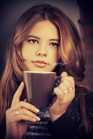 Beautiful pensive teenage girl drinking coffee and looking to the window. Youth style. Loft style interior.の写真素材