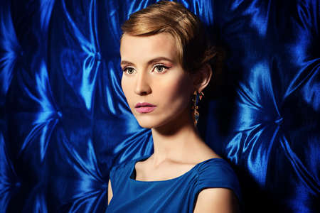 Gorgeous young woman in elegant evening dress standing by a vintage wallpaper. Fashion shot. Retro hairstyle.の写真素材