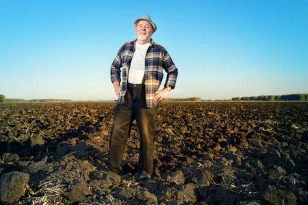 An elderly farmer standing in a plowed field. Agriculture, crop concept.の写真素材