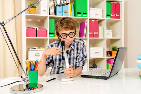 Educational concept. A boy student studying at his workplace with microscope and laptop.の写真素材