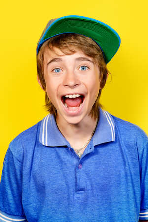 Portrait of a shouting teenage boy over yellow background. Studio shot. Teenager awkward age.の写真素材