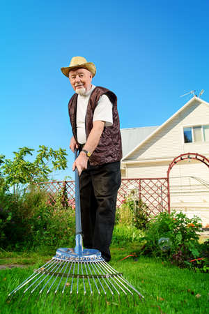 Raking in the garden. Happy senior man gardening in retirement.の写真素材