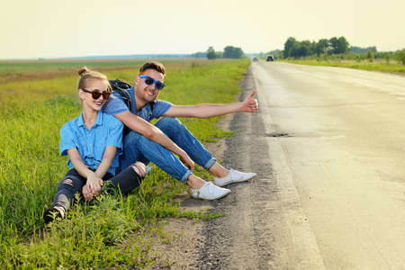 Hitchhiking couple. Happy young people sitting by the highway.の写真素材