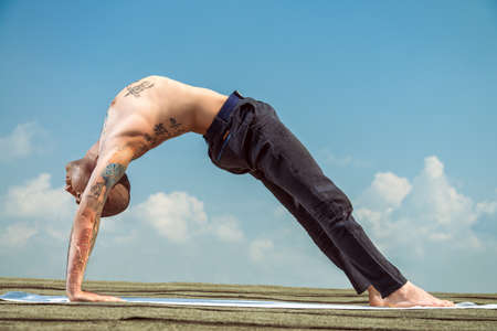 Yoga concept. Experienced yoga master performs various yoga poses on a roof over blue sky.の写真素材
