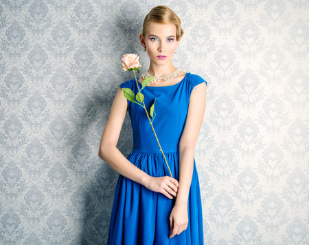 Fashion portrait of a beautiful young woman in  elegant evening dress posing by a vintage wall. Retro Hairstyle.の写真素材